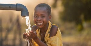 Mali,Kenya - Agust 23 2021:happy boy drinking water from water pump, water well in village in africa.